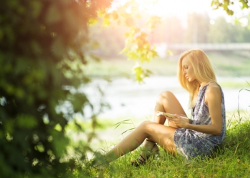 Beautiful sexual blond woman sitting outdoor with book in summer on green natural background, horizontal picture