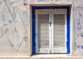 54216496 - blue framed window with white closed shutter. wall of the house with partly covered graffiti. plaka, athens, greece.