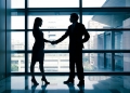 27342987 - successful business woman and man handshaking with office building