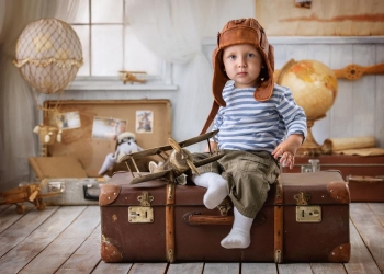 Little boy is himself an aviator and plays with the airplane sitting on a suitcase