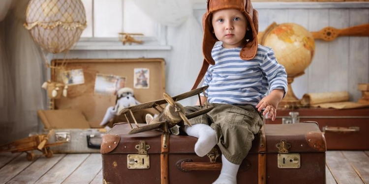 Little boy is himself an aviator and plays with the airplane sitting on a suitcase