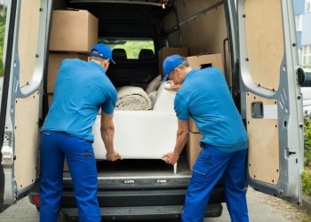 Two Male Workers In Blue Uniform Adjusting Sofa In Truck