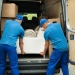 Two Male Workers In Blue Uniform Adjusting Sofa In Truck