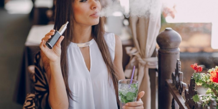 beautiful brunette smoke electronic cigarette on the summer terrace of restaurant