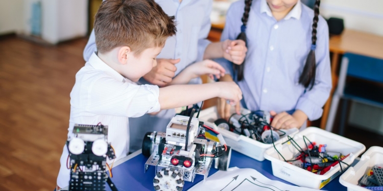 Excited little kid and two smiling teen friends construct robotic toys while playing during their leisure time in technical workshop. Intelligent activity.